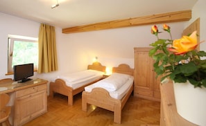 Une chambre à coucher avec deux lits en bois, un bureau avec un ordinateur, une armoire et une fenêtre avec des rideaux.
