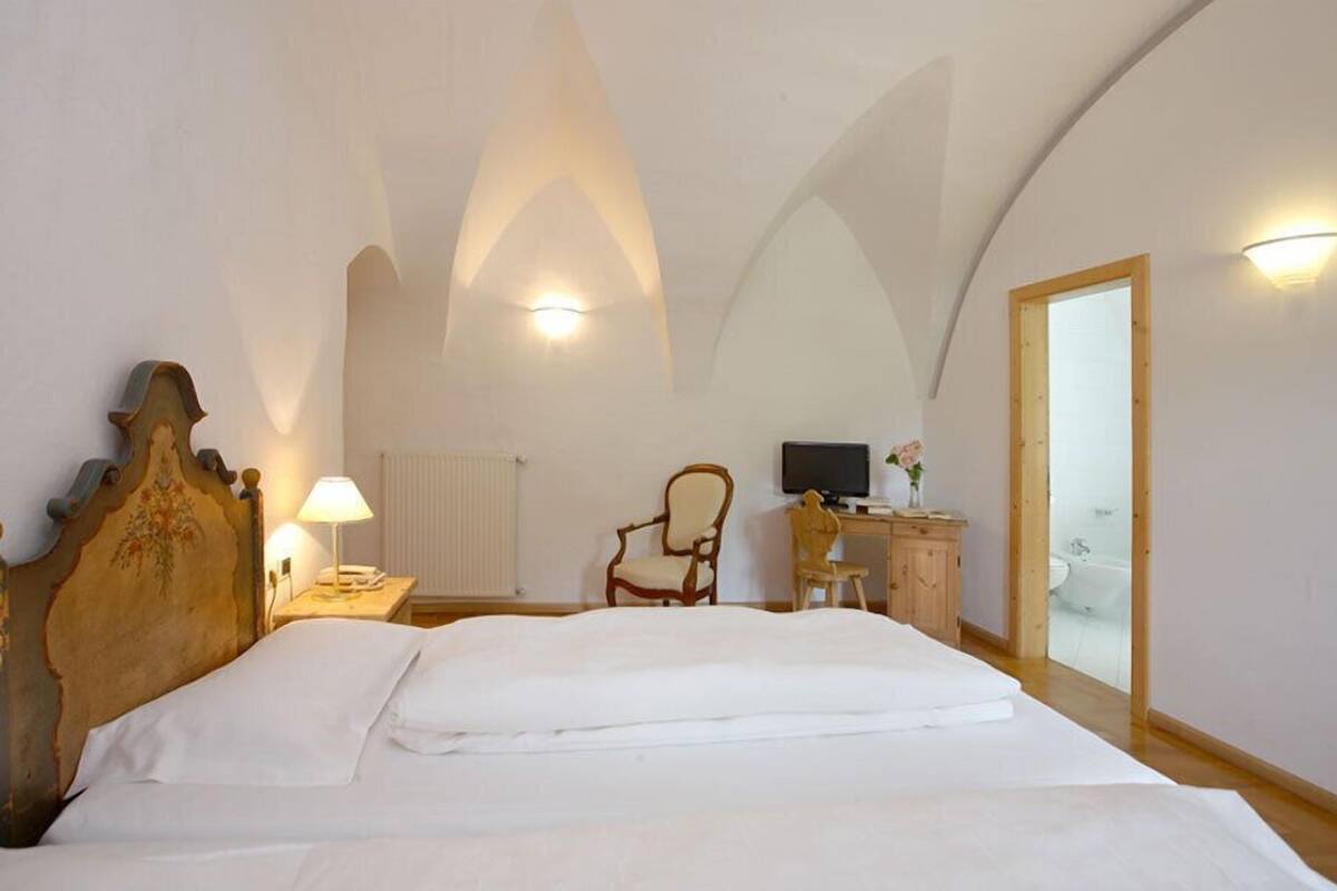Una camera da letto con un letto grande, una testiera in legno, una scrivania con un computer, una sedia e vista su un paesaggio innevato attraverso una porta vetrata.