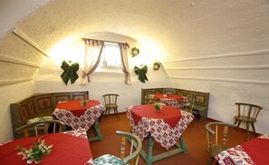 Un coin repas accueillant avec quatre tables, chacune recouverte d’une nappe rouge et entourée de chaises en bois.