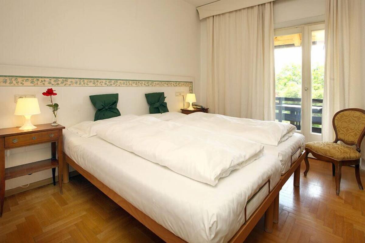 Una camera d'albergo con un letto grande, due comodini con lampade, una sedia e vista sull'esterno.