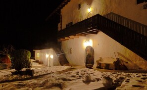 Un bâtiment dont la cour est recouverte de neige, avec un escalier et une entrée illuminée.