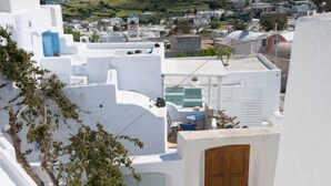Un bâtiment aux murs blancs, doté d’une porte en bois, d’une piscine bleue et offrant une vue sur une ville côtière.