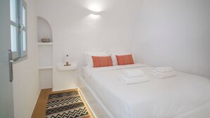 Une pièce blanche avec un lit, une table de chevet, une étagère et un tapis à motifs.