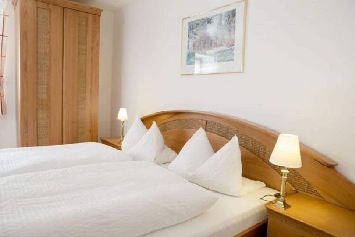 Una cama doble con ropa de cama y almohadas blancas, un cabecero de madera, lámparas de noche y un cuadro enmarcado en la pared.