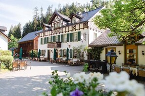 A traditional European-style building with a courtyard, outdoor seating, and a mountain backdrop. - Gasthof Bischofsmühle (Helmbrechts)