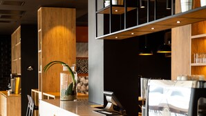 A modern bar area with wooden bar counter, black bar stools, and potted plants on shelves. - Park Inn by Radisson Vilnius Airport Hotel & Conference Centre (Vilnius)