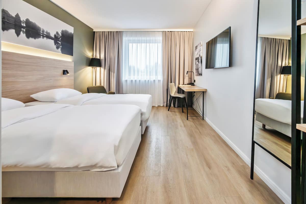 A hotel room with two beds, a desk, a chair, and a large window with curtains.
