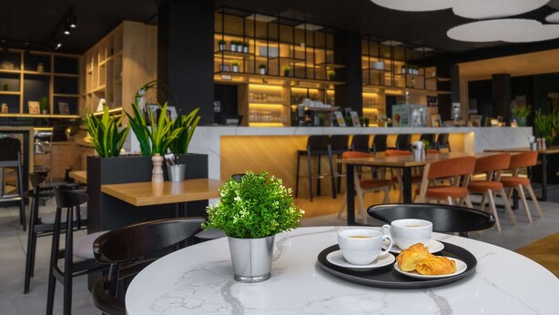 A modern cafe with a marble table, a small potted plant, a cup of coffee, and a plate of pastries. - Park Inn by Radisson Vilnius Airport Hotel & Conference Centre (Vilnius)