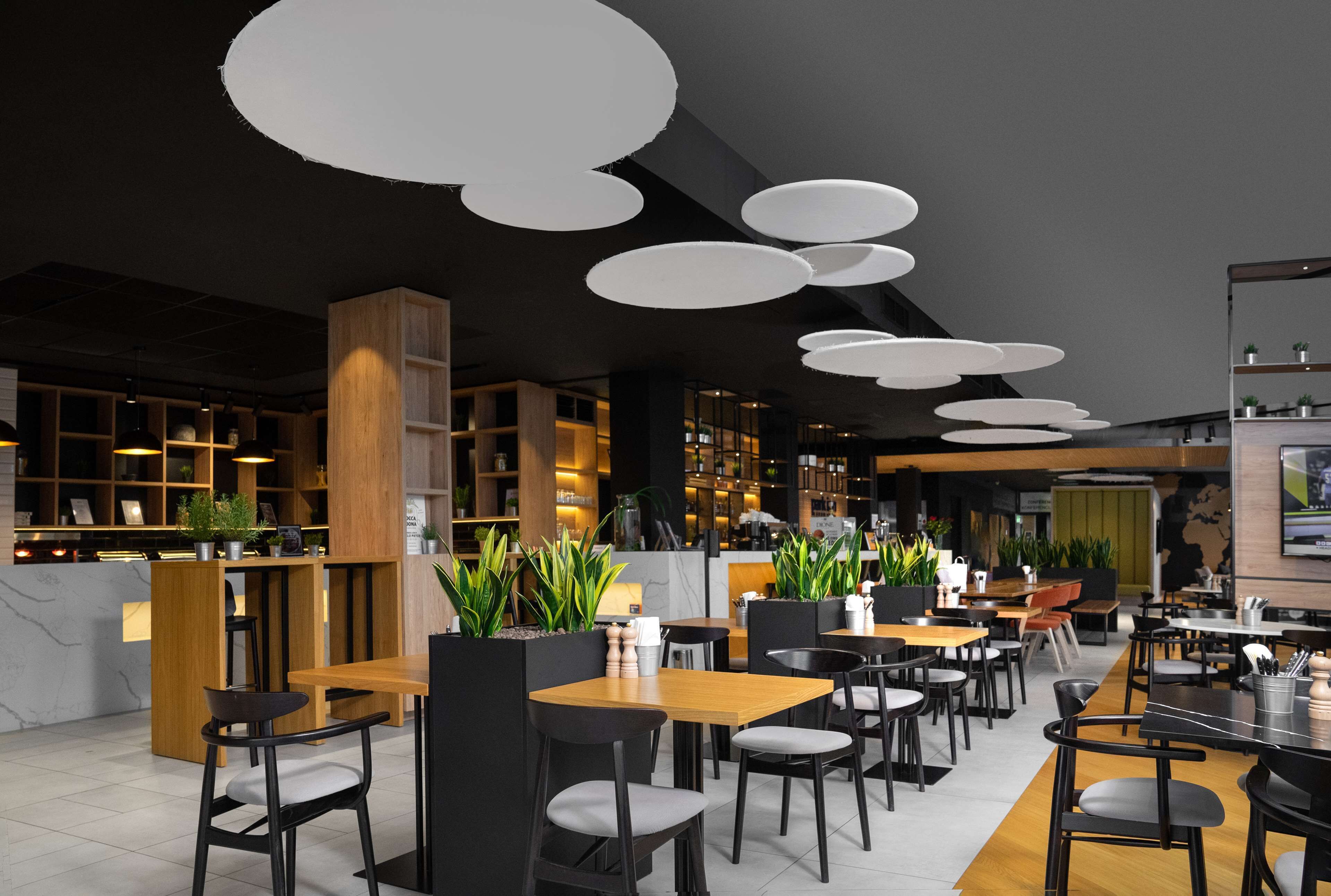 A modern restaurant interior with wooden tables and chairs, pendant lighting, and potted plants.