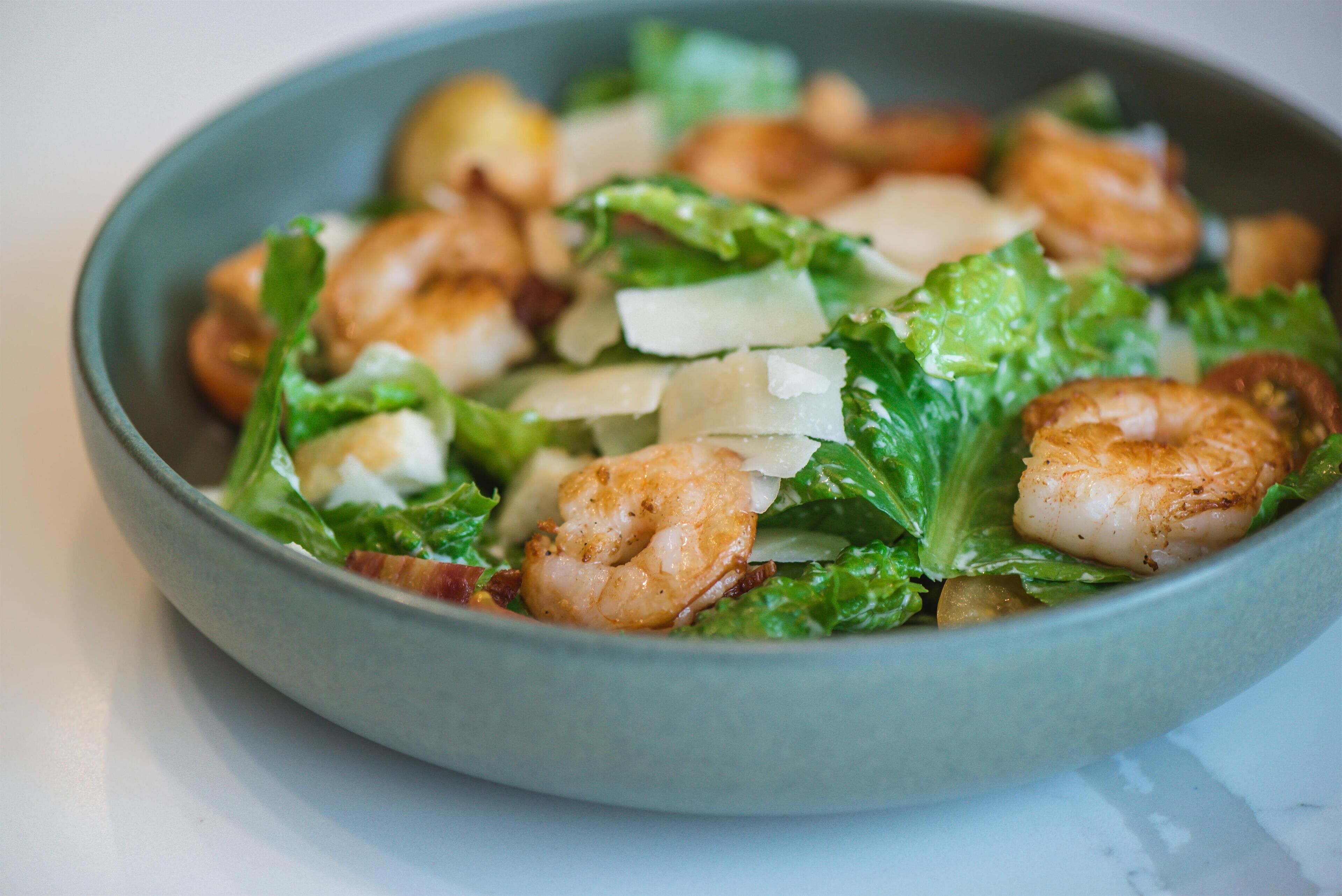 A bowl of salad with shrimp, lettuce, and cheese.