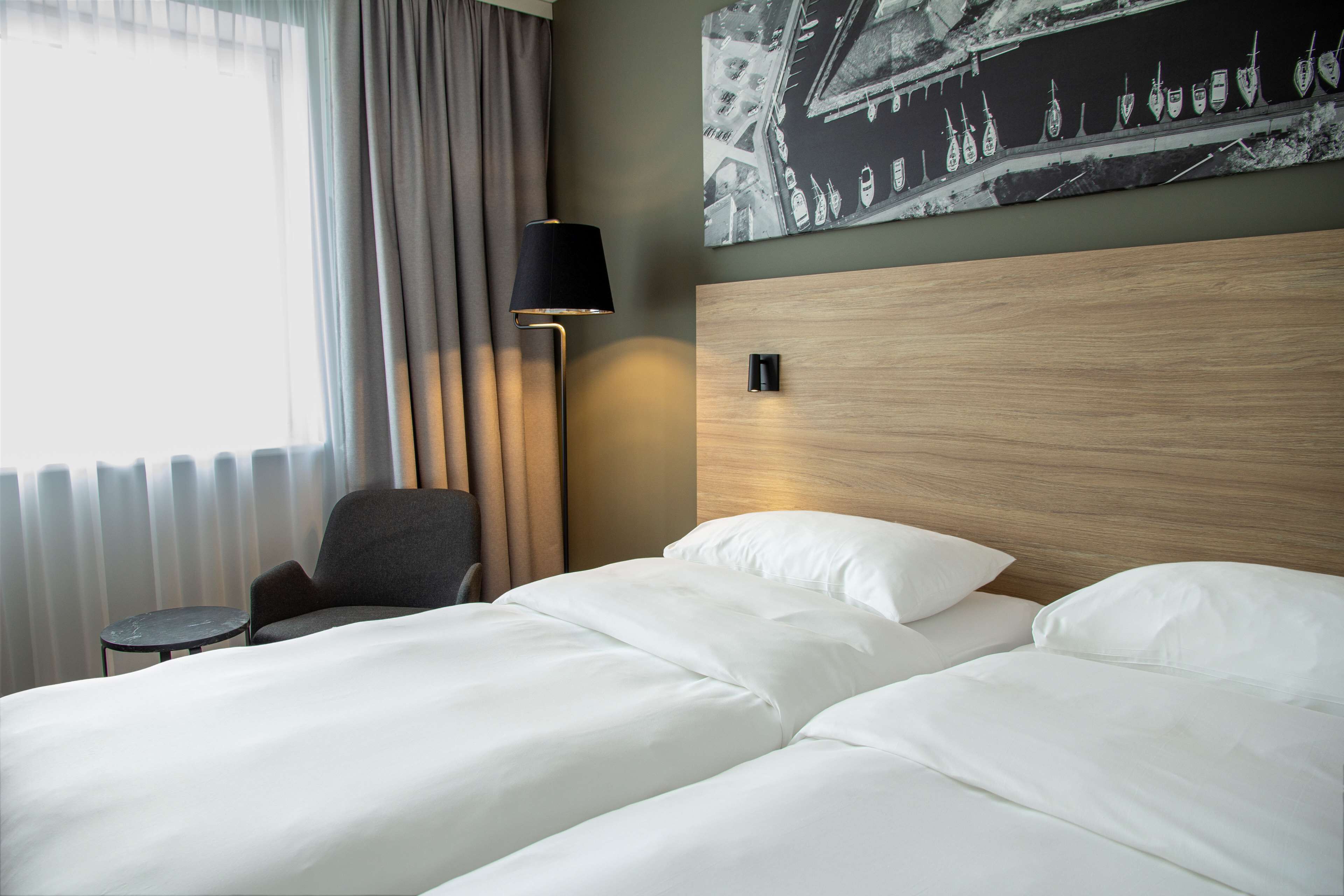 A hotel room with a bed, a chair, a lamp, and a wall-mounted light fixture.