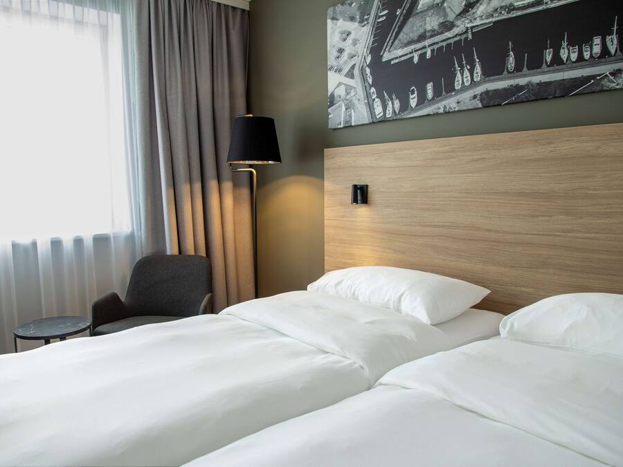 Une chambre d’hôtel avec un lit, une chaise, une lampe et un luminaire fixé au mur.