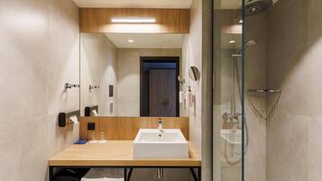 Un baño moderno con tocador de madera, un espejo grande, un lavamanos blanco y una zona de ducha con mampara de cristal.