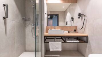 Un baño moderno con ducha envuelta en vidrio, tocador de madera con lavamanos y un perchero para toallas.