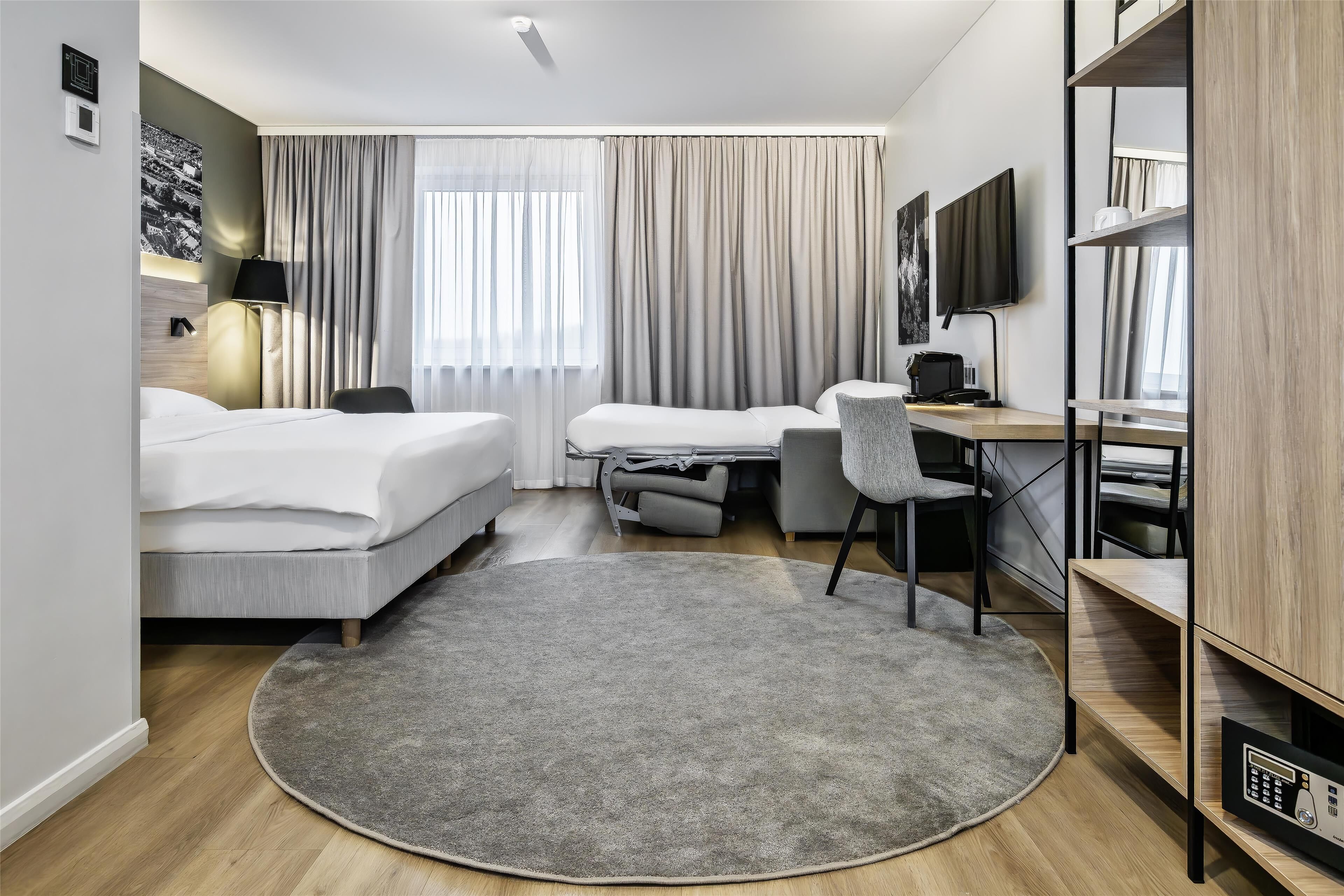 Una habitación de hotel moderna con una cama, escritorio, silla y un tapete grande.