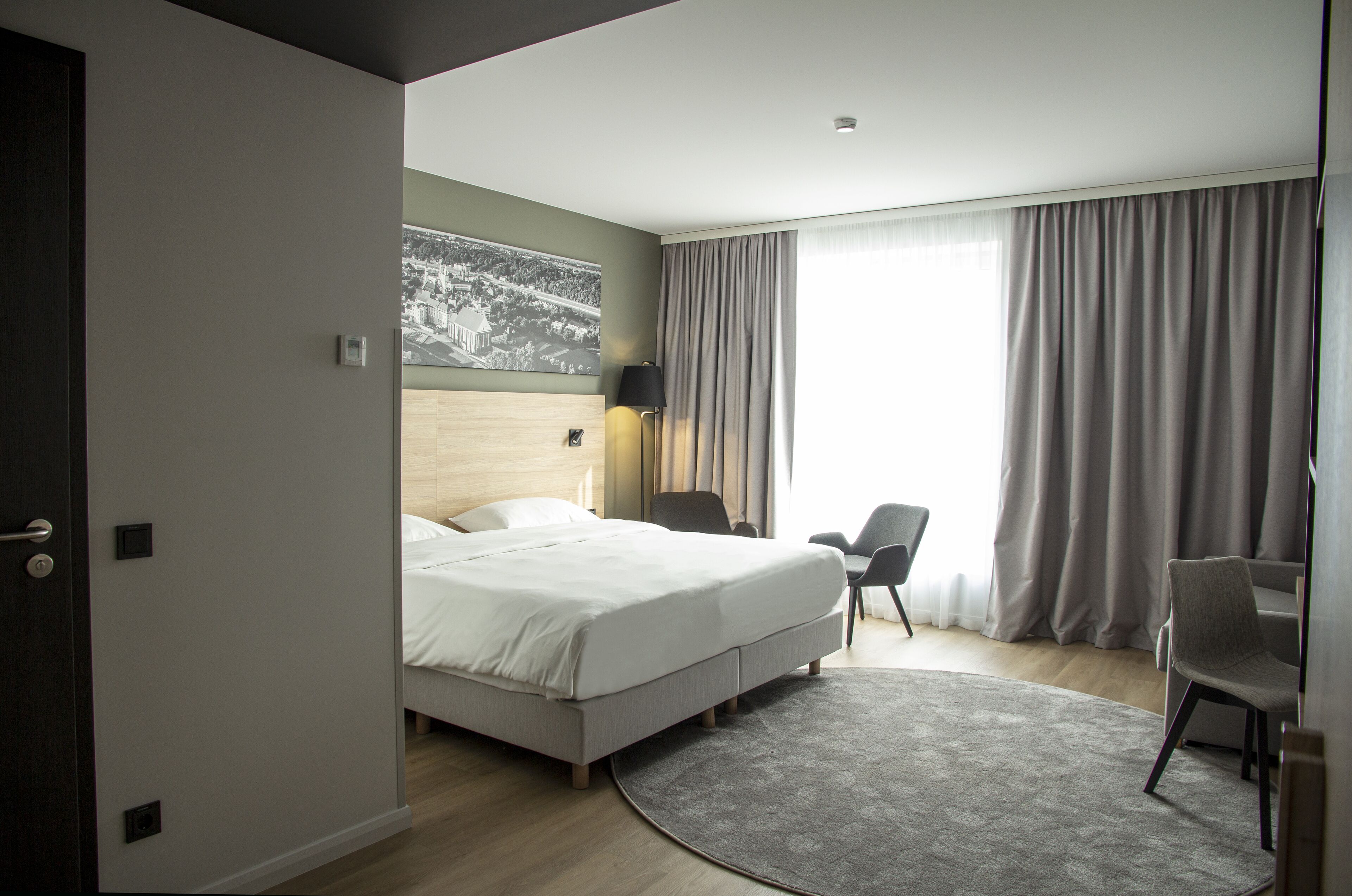 Habitación de hotel moderna con una cama grande, un escritorio, una silla y vistas a un paisaje urbano a través de la ventana.
