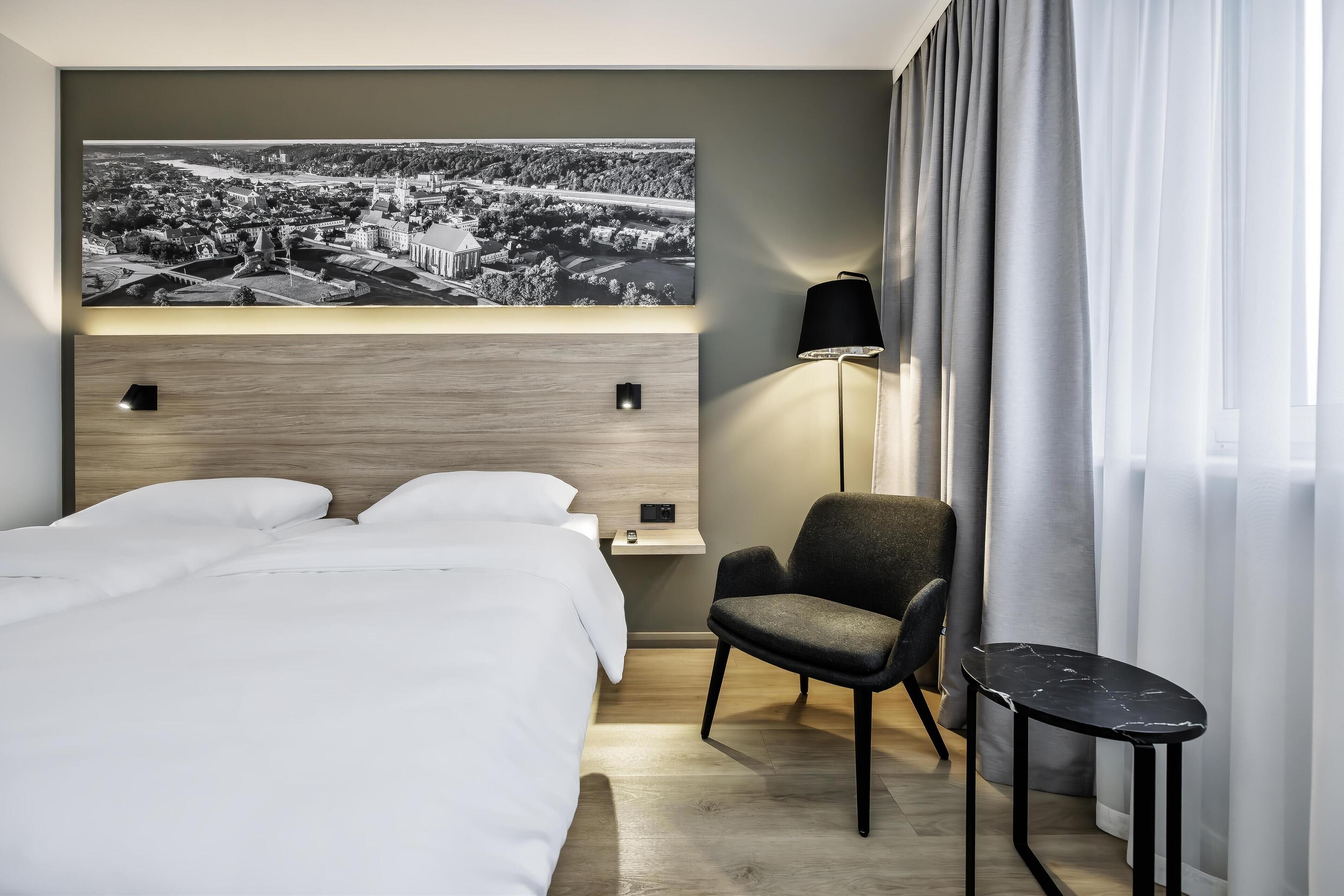 A modern hotel room with a large bed, a desk, a chair, and a small table.