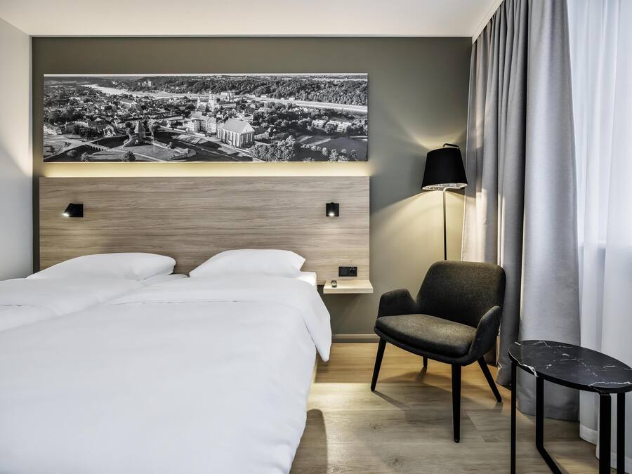 A modern hotel room with a large bed, a desk, a chair, and a small table.