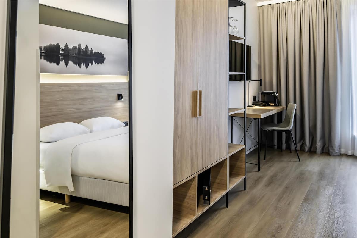 A hotel room with a bed, a desk, a chair, and a large window with curtains.