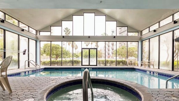A modern indoor swimming pool with clear glass walls, a hot tub, and lounge chairs. - 2 BR RESORT IN PERFECT LOCATION NEAR UNIVERSAL (Orlando)