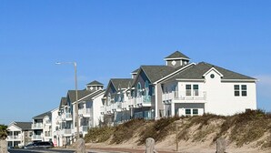 Una hilera de casas de playa con balcones, una playa de arena y un cielo azul despejado.