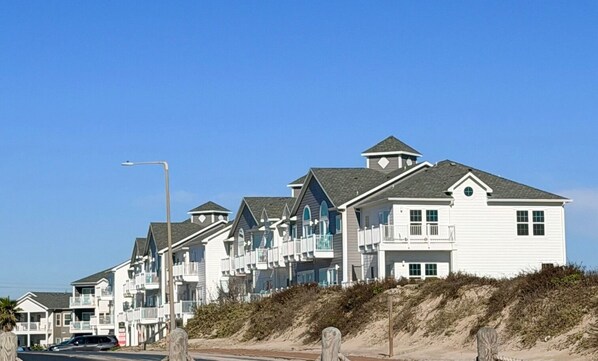 A row of beach houses with balconies, a sandy beach, and a clear blue sky.