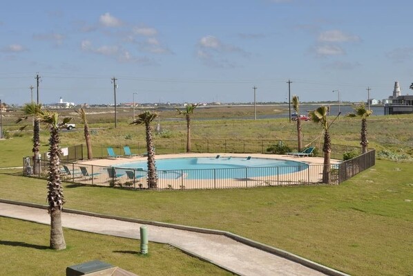 Una piscina con área cercada, palmeras y vista a un faro y una masa de agua.