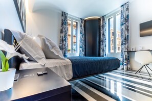 A modern hotel room with a large bed, a desk with a laptop, a potted plant, and a view of the city through large windows. - V-Accommodation IV Fontane (Rome)