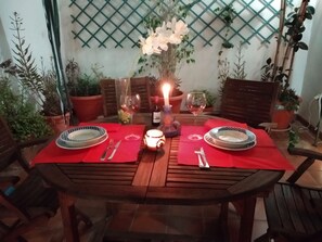 A wooden dining table set for two with red placemats, white plates, and wine glasses.