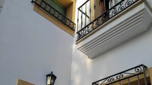 Un edificio de dos pisos con una puerta marrón, una pared blanca y una ventana con barrotes.