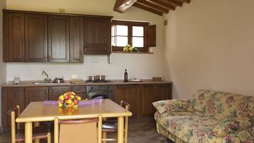 Una cocina con armarios de madera, una mesa de comedor con sillas, un sofá floral y una ventana con flores.