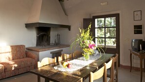 A cozy living room with a fireplace, a dining table with chairs, a sofa, and a television. - Castello di Modanella (Rapolano Terme)
