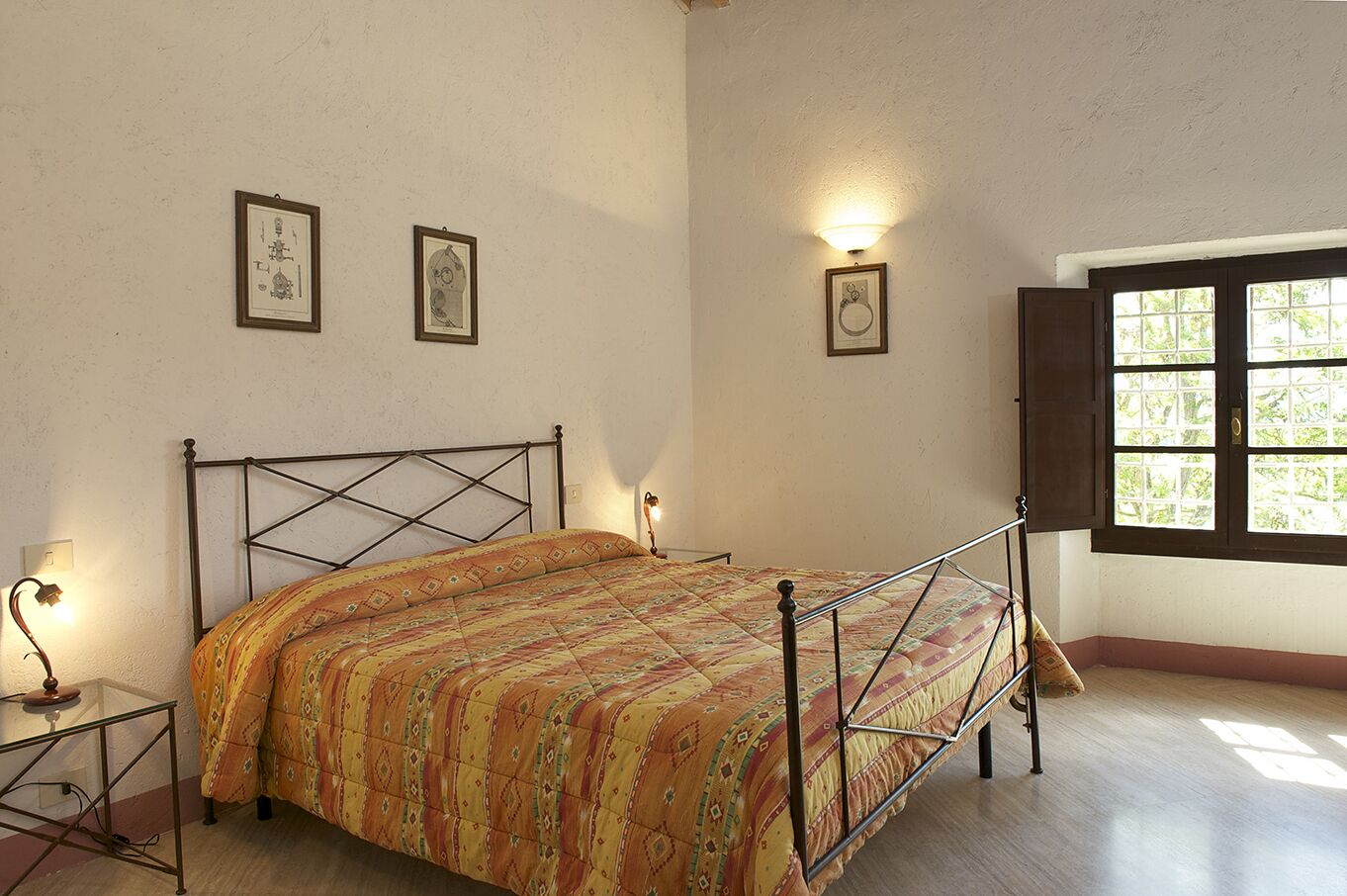 Un dormitorio con cama, mesita de noche, lámpara y ventana con vistas al verdor.