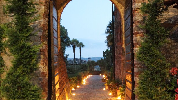 An arched stone gateway leading to a pathway lined with potted plants and lights. - Castello di Modanella (Rapolano Terme)
