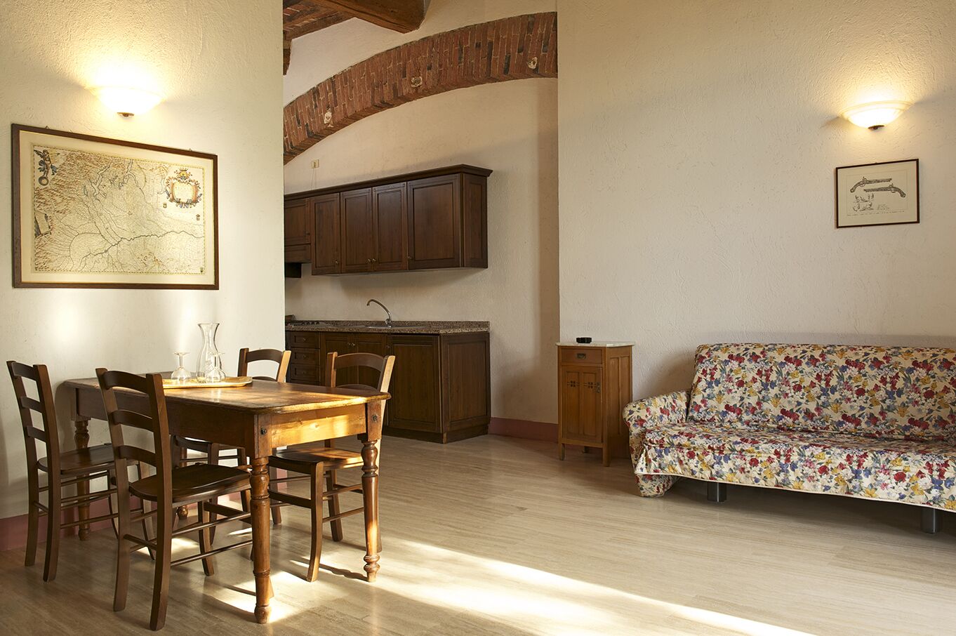 A dining area with a wooden table and chairs, a sofa, and a kitchen in the background.