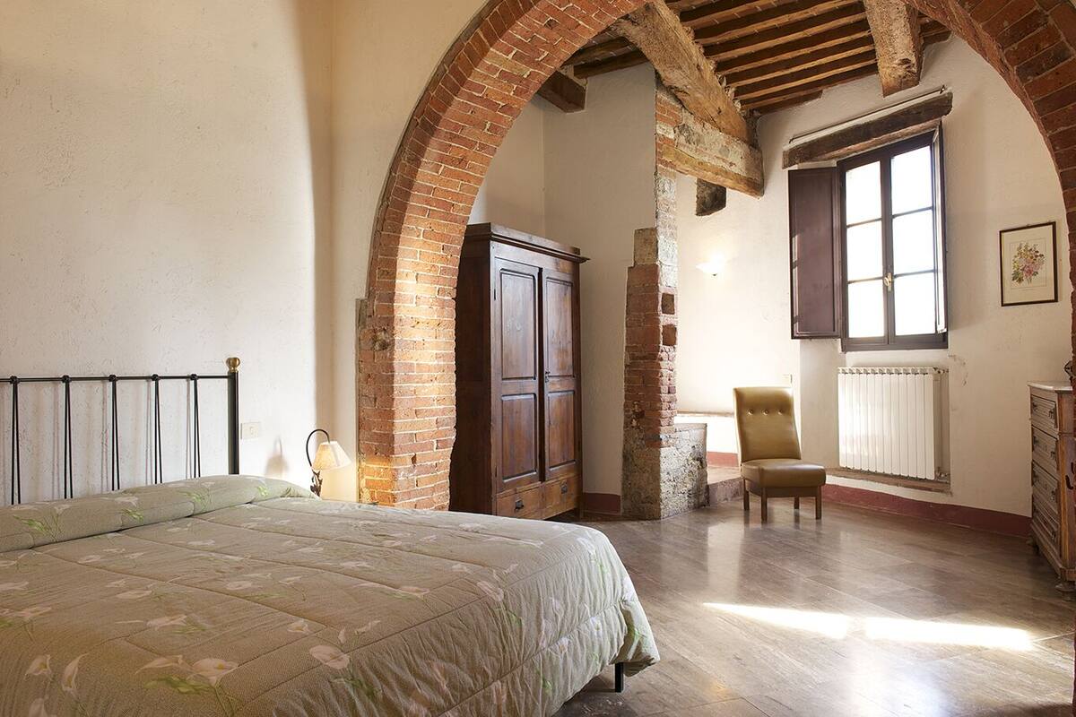 A bedroom with a bed, a chair, a wardrobe, and a window.