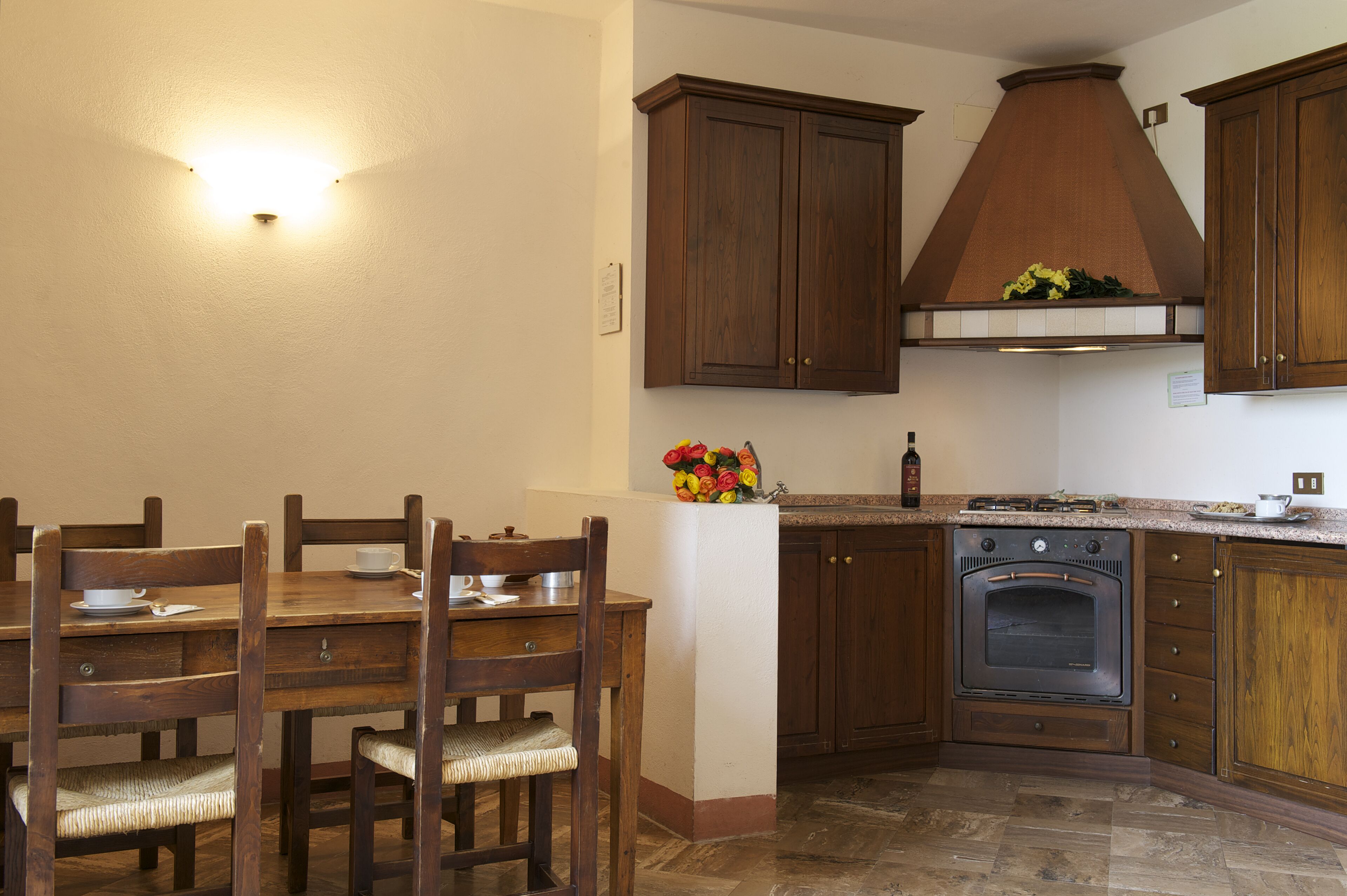 Una cocina con armarios de madera, horno empotrado y una mesa de comedor con sillas.
