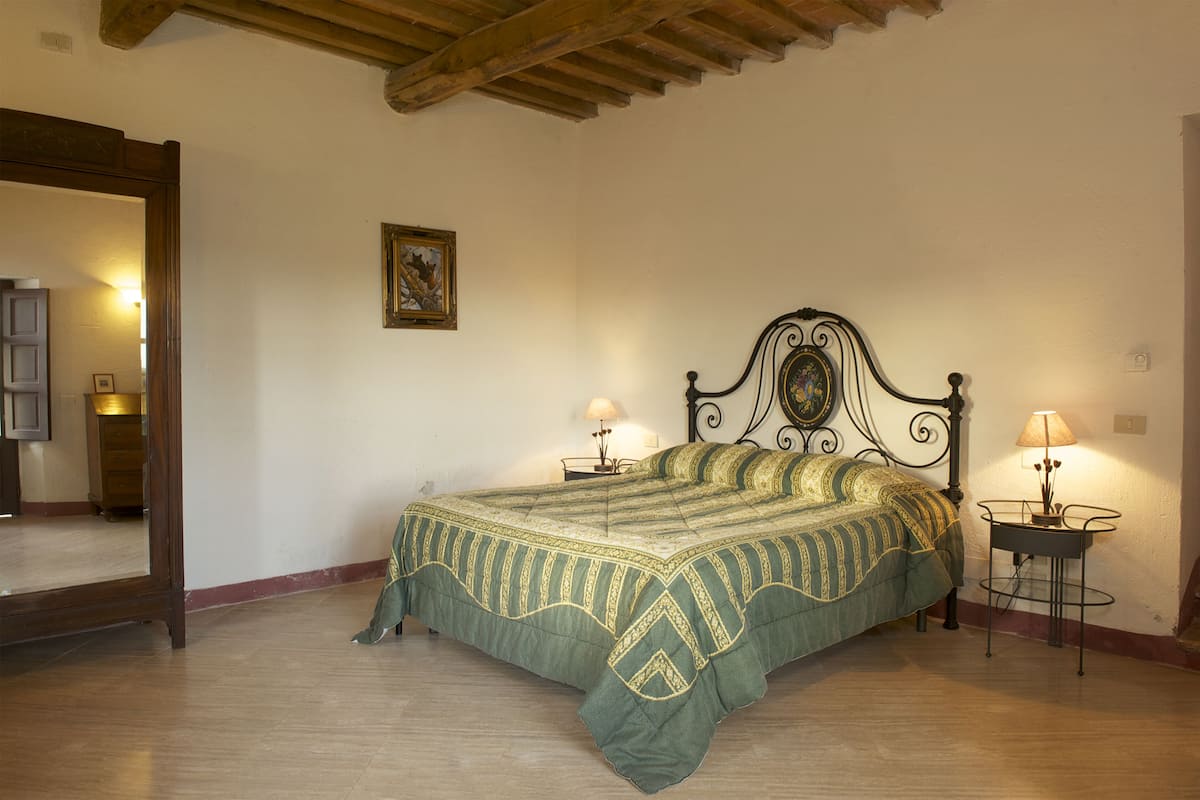 A bedroom with a bed, two bedside tables, a mirror, and a framed picture on the wall.