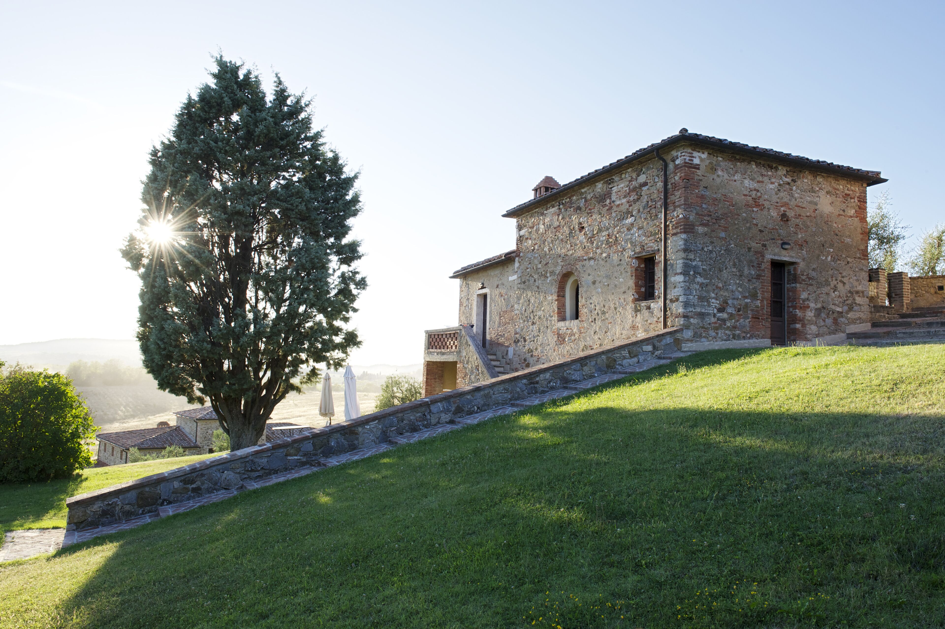 A stone building with a sloped roof, a staircase leading to the entrance, and a tree in the foreground.