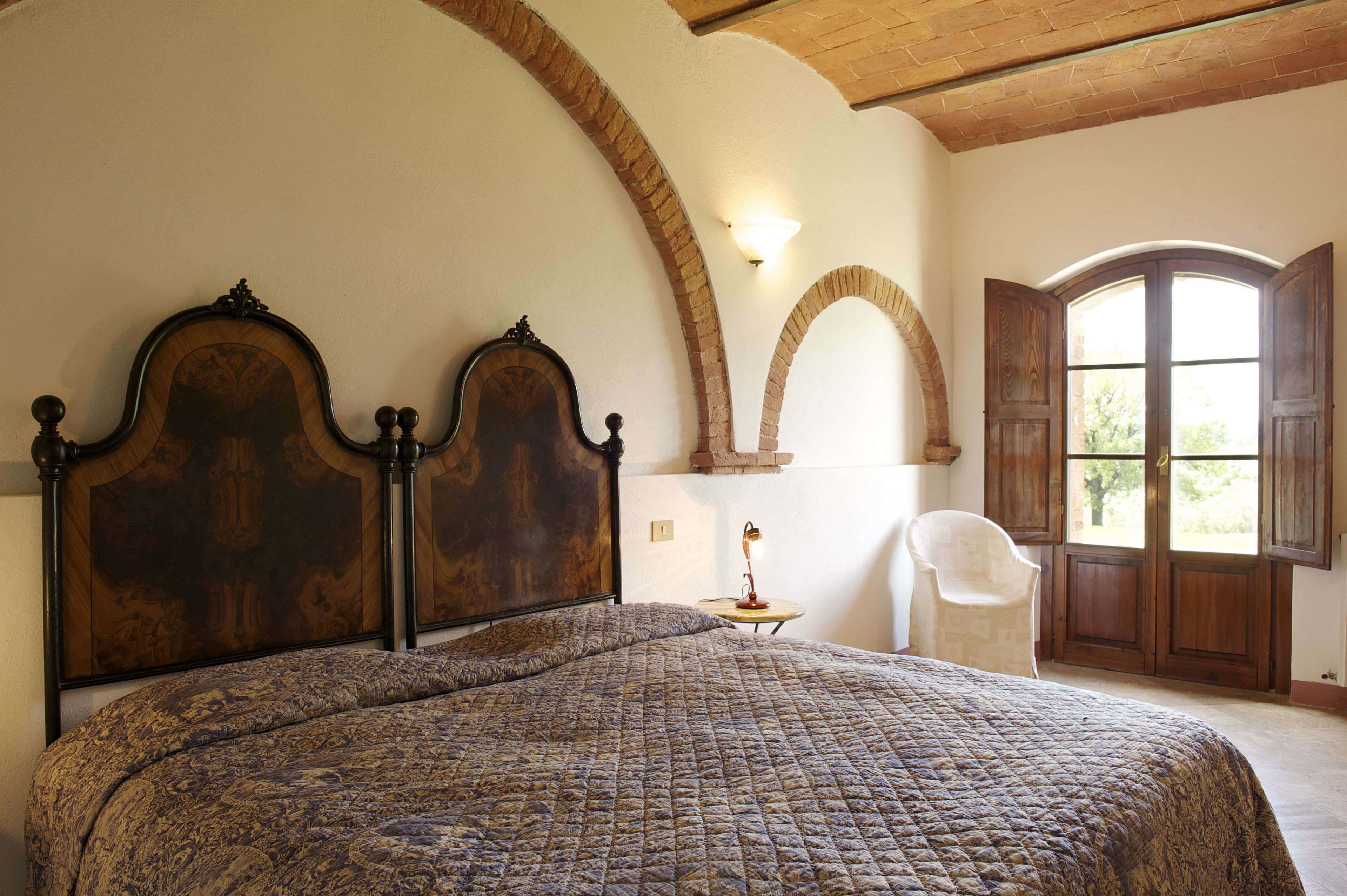 Un dormitorio con una cama grande, una silla y una ventana con contraventanas de madera.