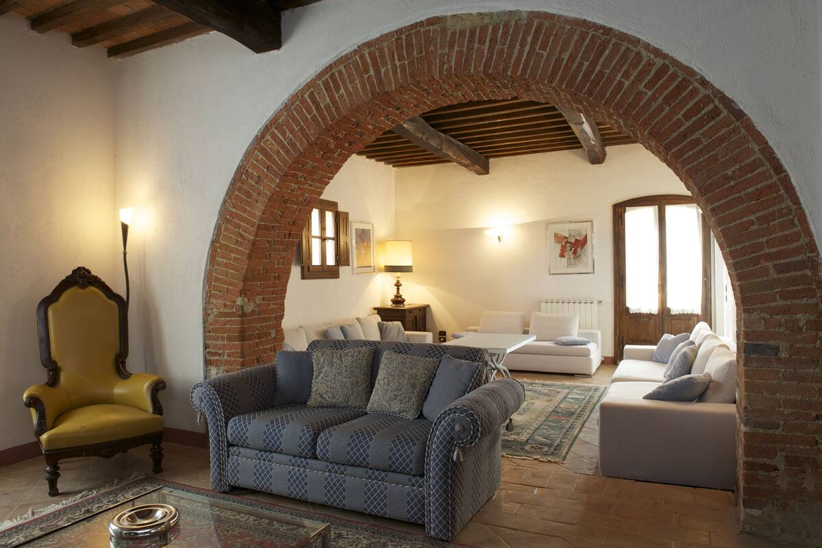 A living room with a brick archway, a yellow armchair, a patterned sofa, and a white sofa.