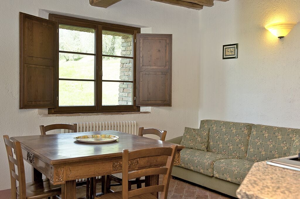 Un comedor con una mesa y sillas de madera, una ventana con contraventanas de madera, un radiador y un sofá verde.