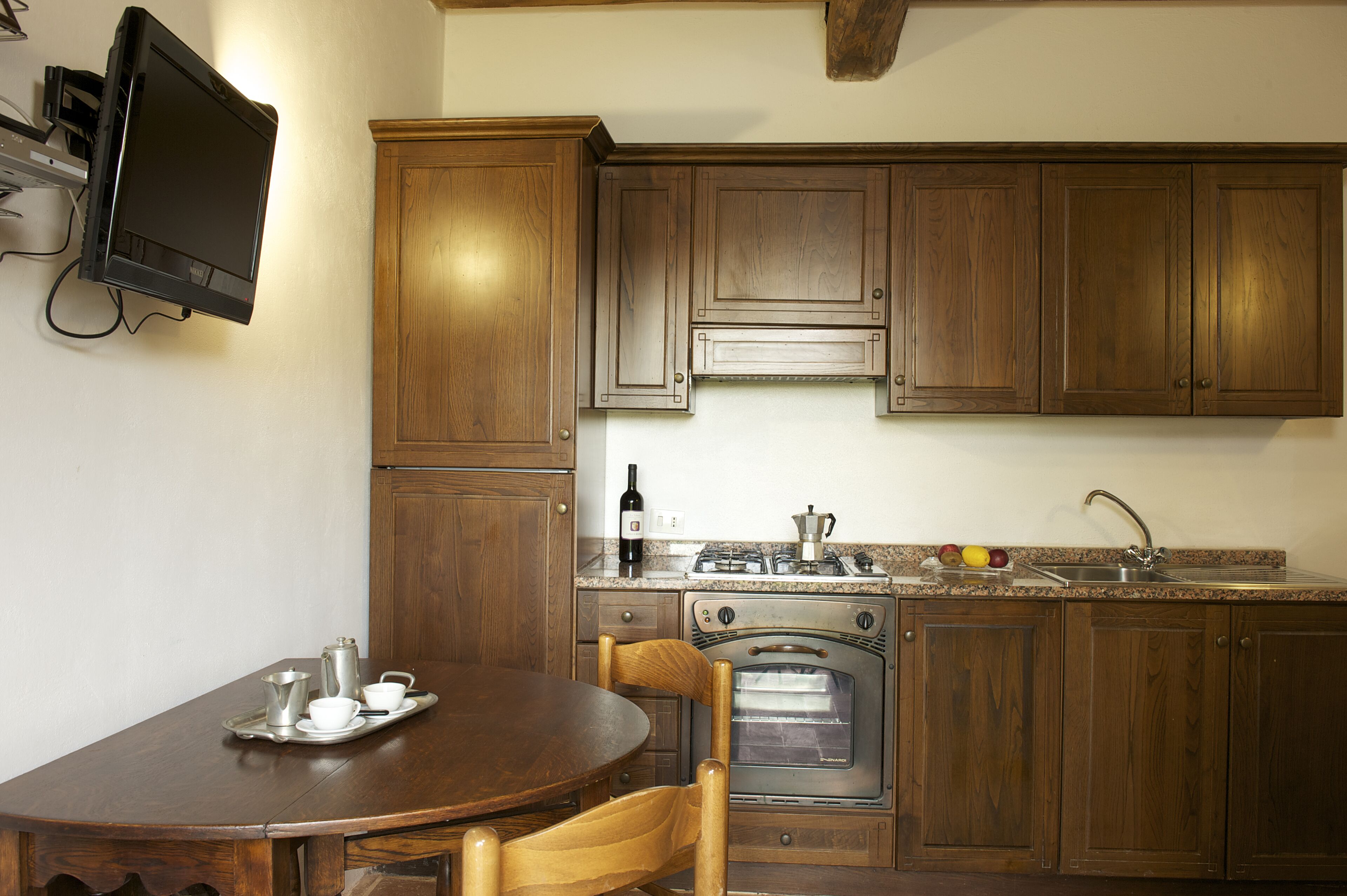 A kitchen with wooden cabinets, a stove, an oven, a sink, and a television mounted on the wall.
