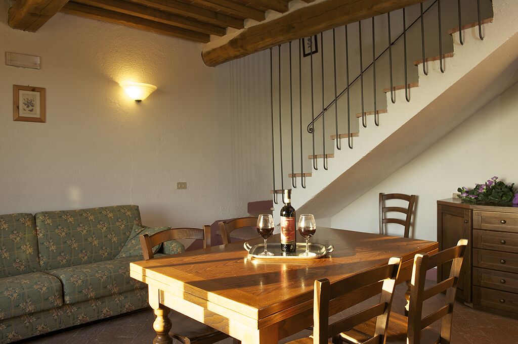 A dining area with a wooden table set for two, a sofa, and a staircase with a metal railing.