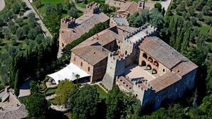 An aerial view of a historic castle complex with multiple buildings, including a large central structure with a tower, surrounded by well-maintained gardens and pathways. - Castello di Modanella (Rapolano Terme)