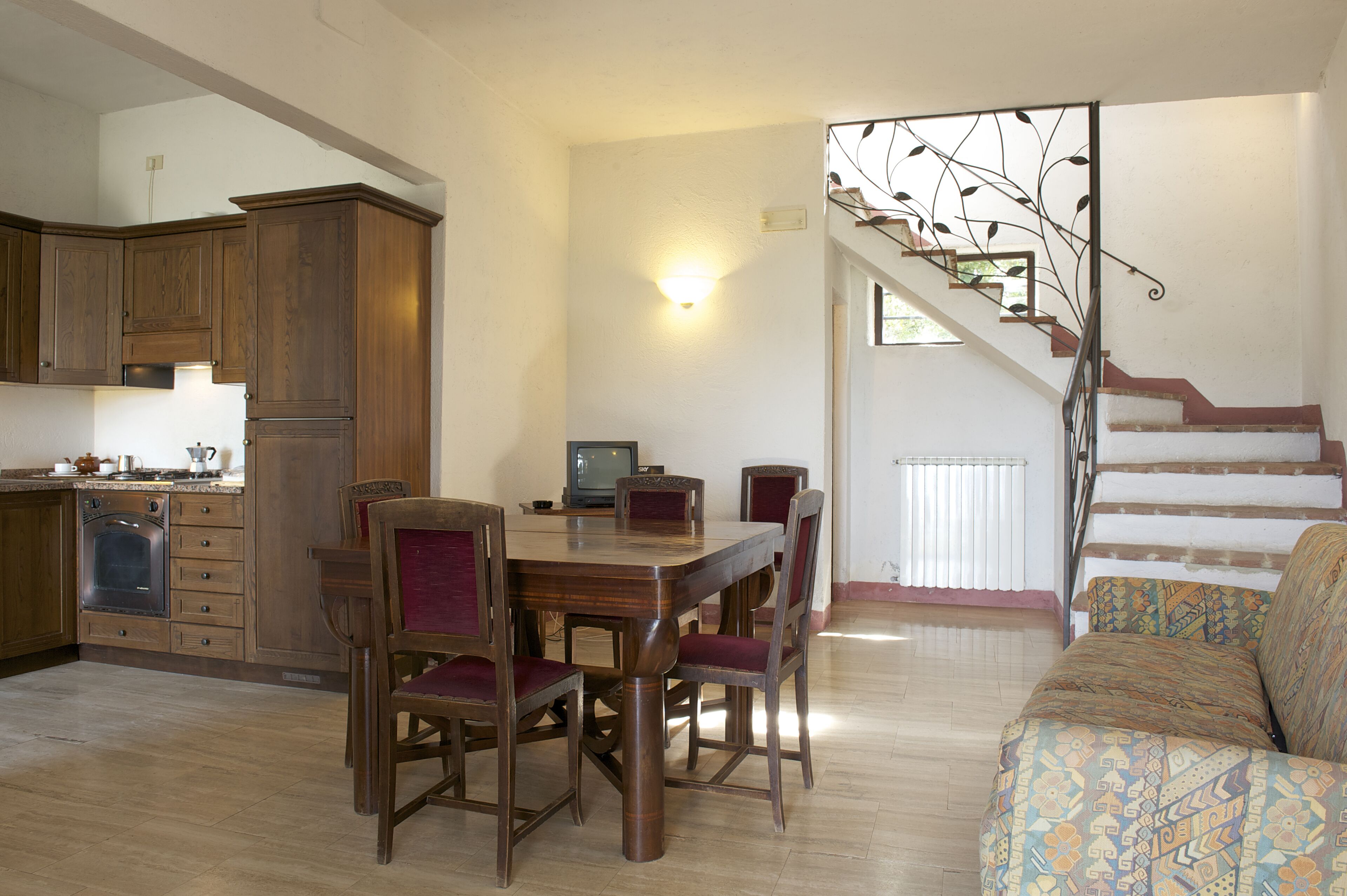 Un comedor con una mesa y sillas de madera, una cocina con armarios de madera y una escalera con barandilla de metal.