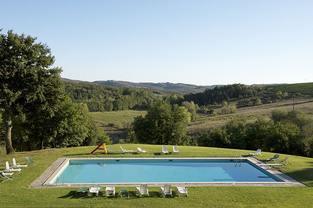 Une piscine rectangulaire à l’eau d’un bleu limpide, entourée d’une pelouse où sont disposés plusieurs chaises longues et une petite structure de jeux.