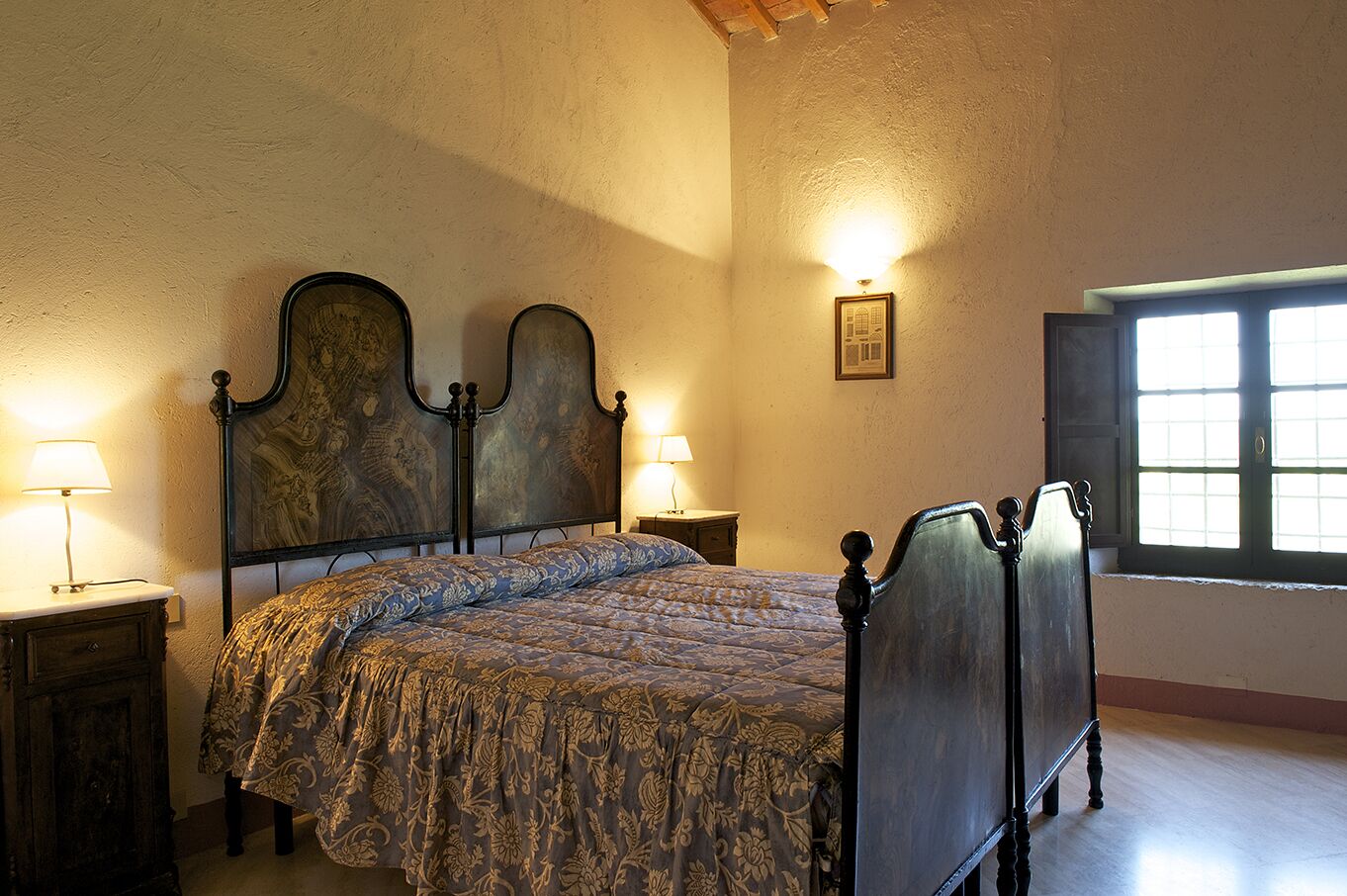 Un dormitorio con una cama grande, dos mesitas de noche con lámparas, un cuadro en la pared y una ventana con persianas.