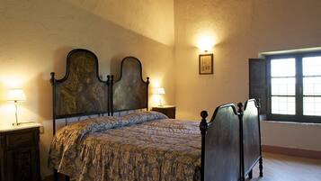 A bedroom with a large bed, two bedside tables with lamps, a framed picture on the wall, and a window with blinds.