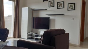 Ein modernes Wohnzimmer mit Flachbildfernseher, einer Couch und einem Couchtisch. An der Wand hängen drei gerahmte Kunstwerke.